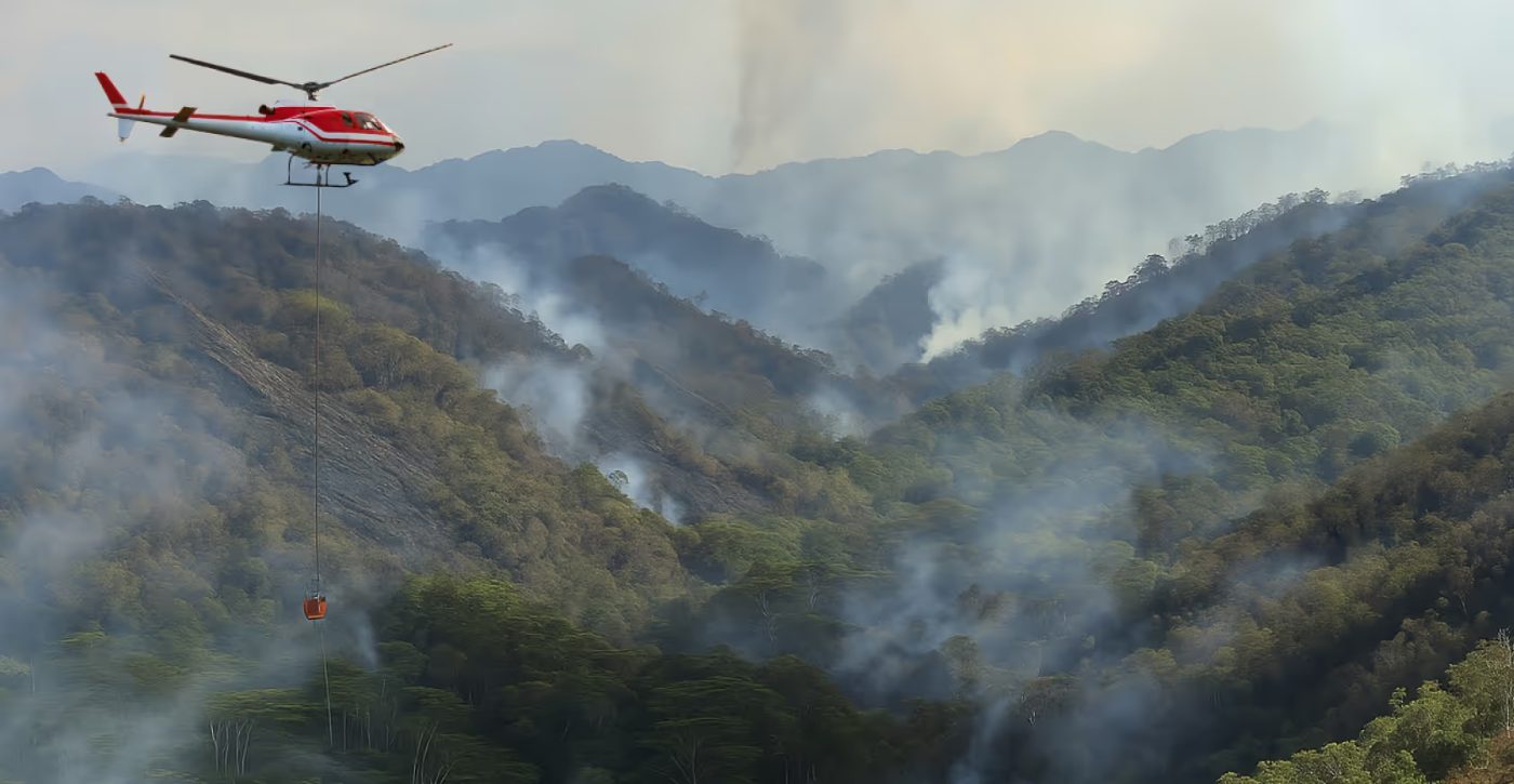 A helicopter flying over a smoking wildfire