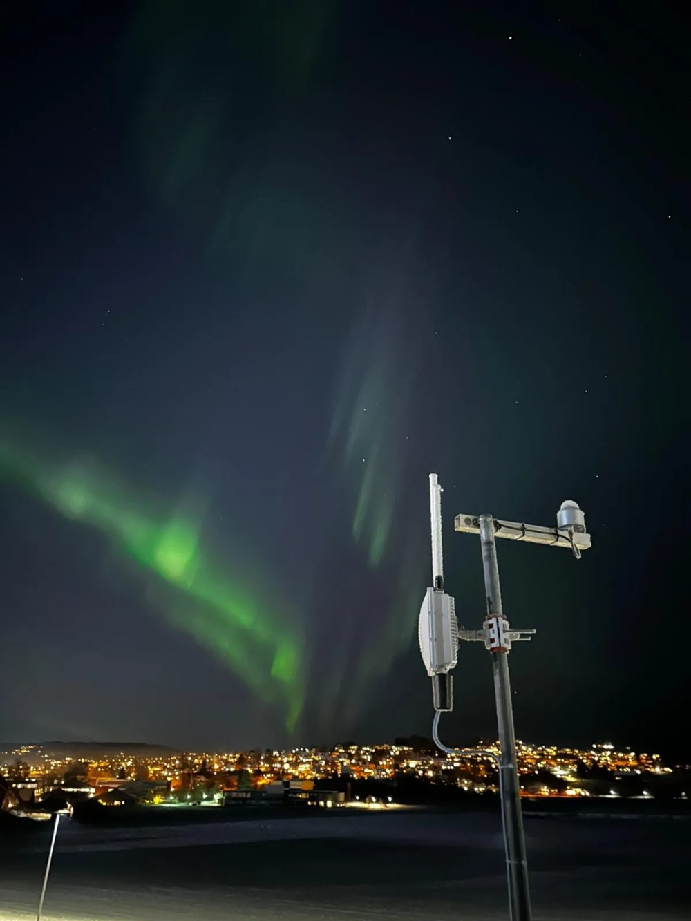 A fixed receiver on a mast at night under the northern lights