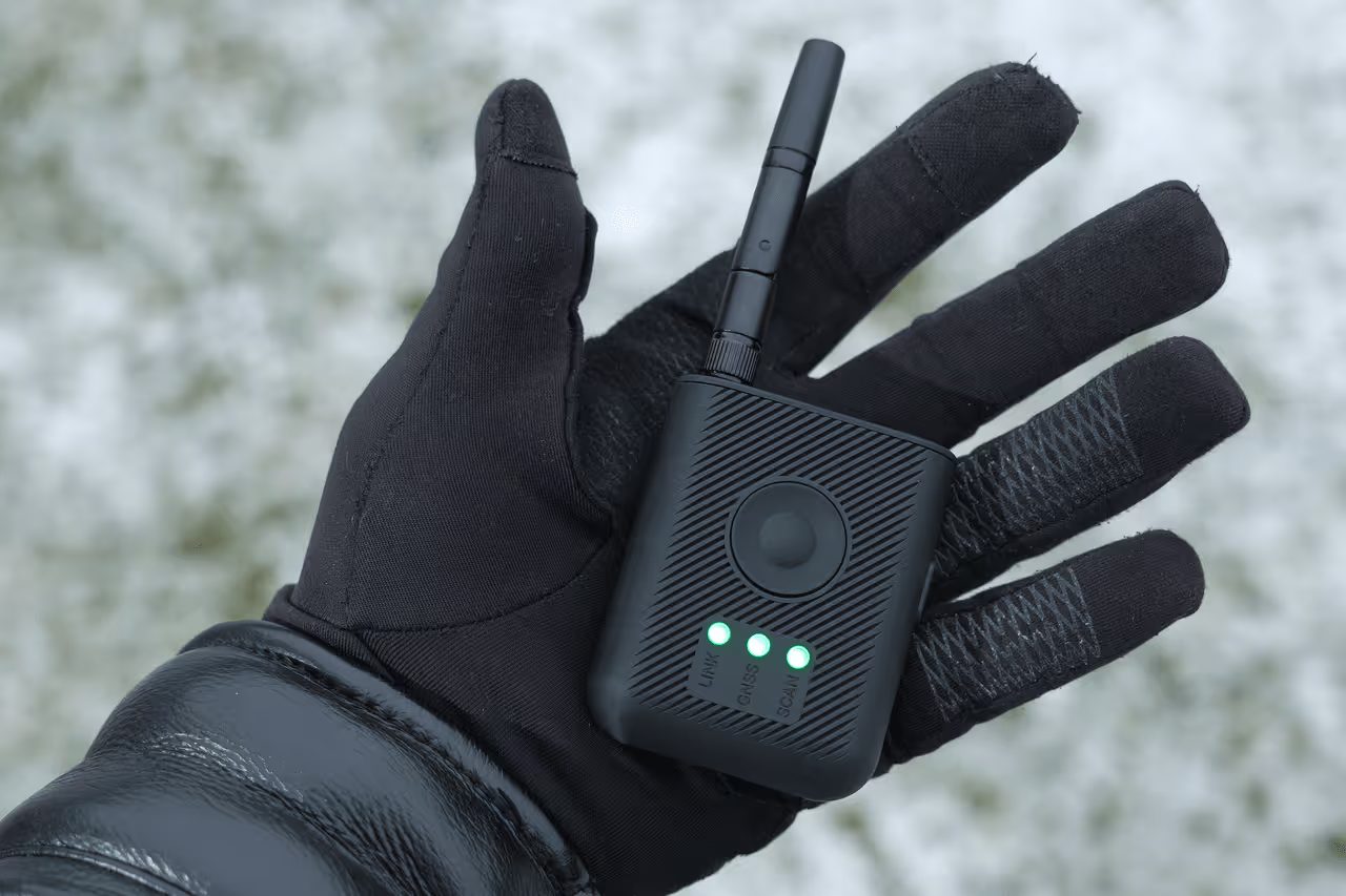 A gloved hand holding a handheld receiver in winter